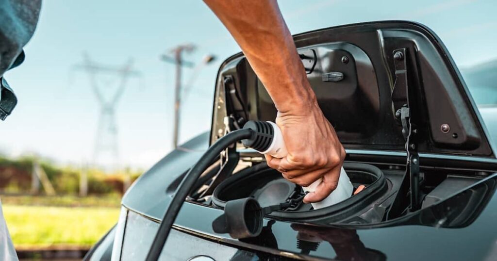 A person plugs in a charging cable into the electric car's charging port.