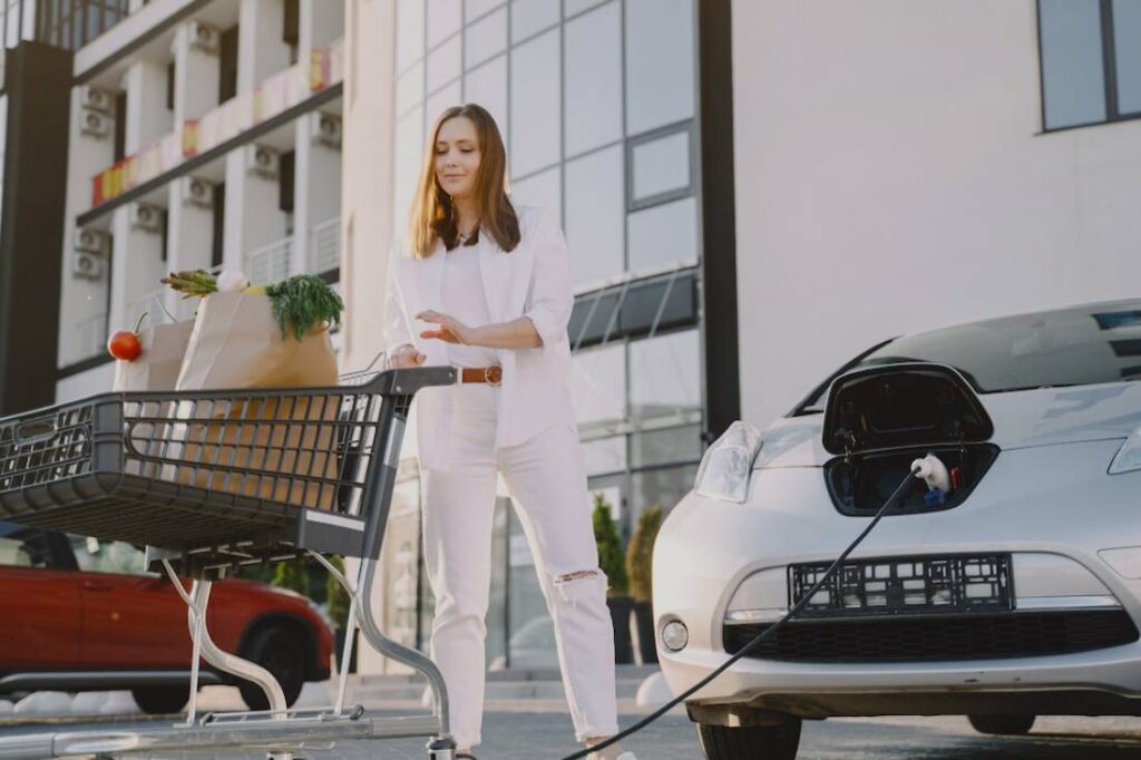 A woman in white attire stands next to an electric car.