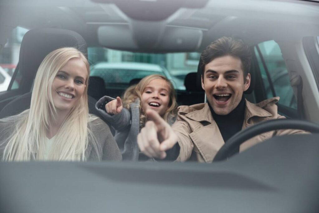 . A family in a car excitedly points at something outside the window while driving.