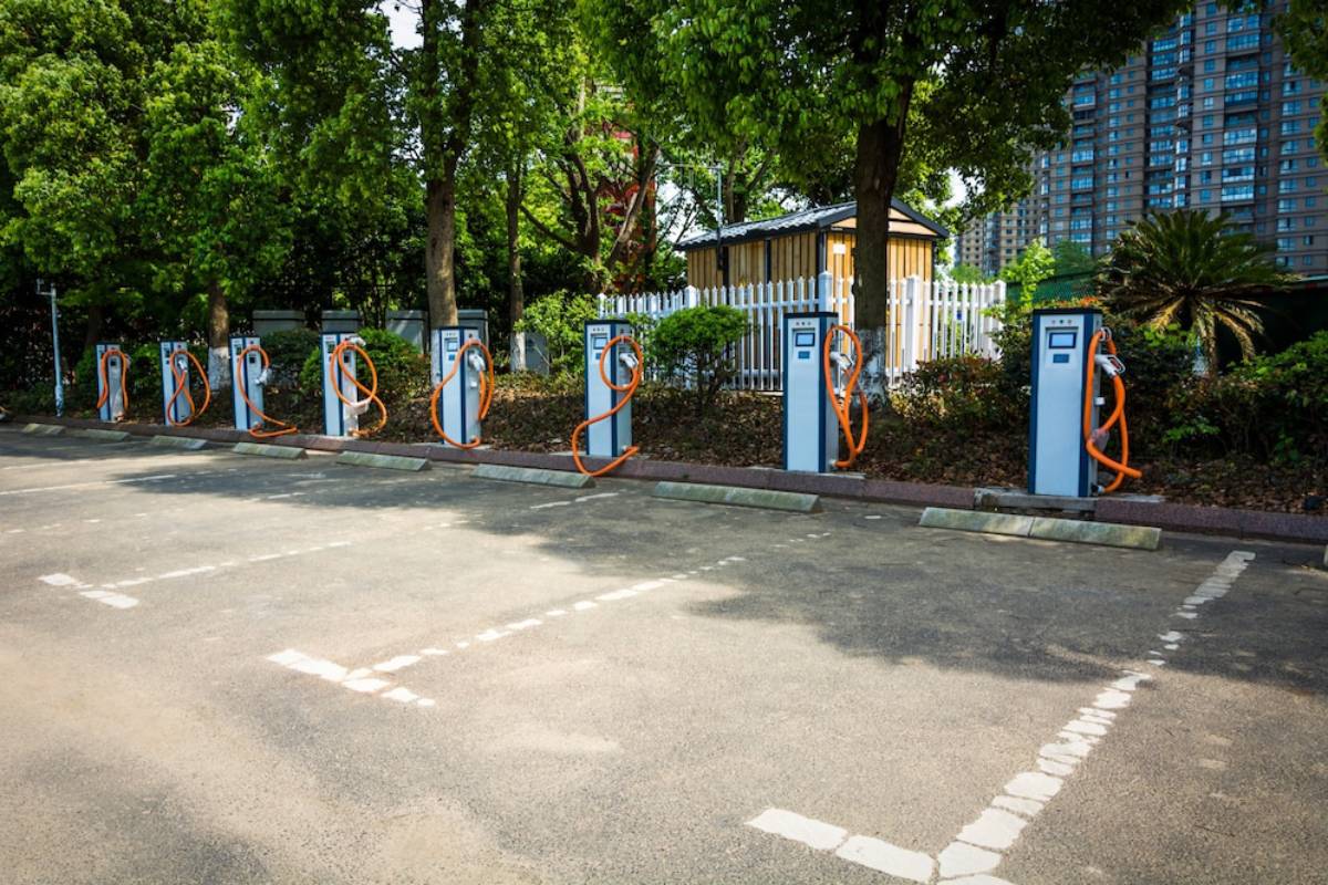  . Electric vehicle charging stations lined up in a parking lot, with several cars parked nearby, ready for charging.