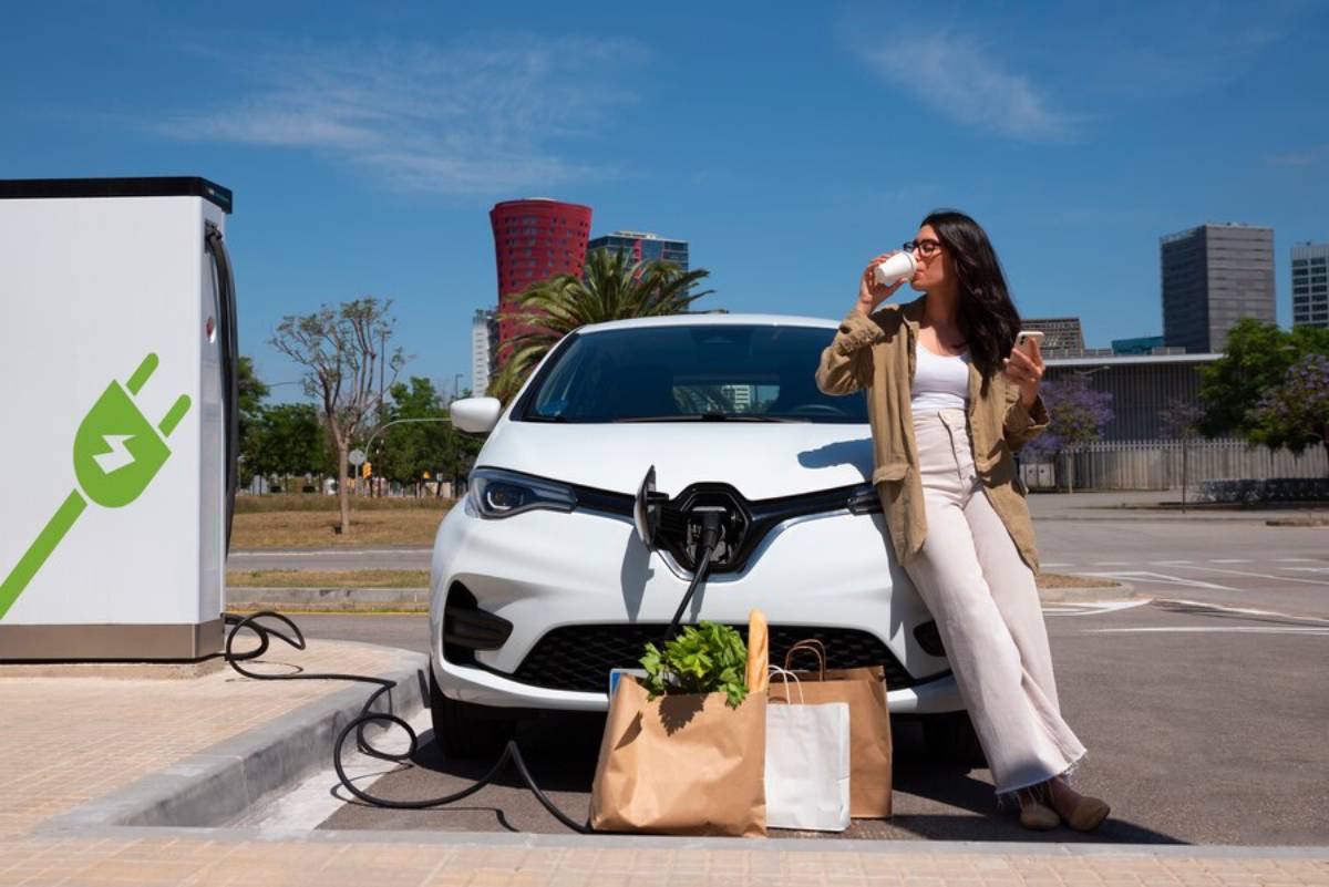  . A woman stands beside her electric car, using her phone to monitor the charging process.
