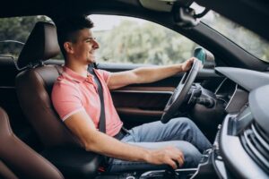 A man seated in the driver's seat of a car, focused on the road ahead.