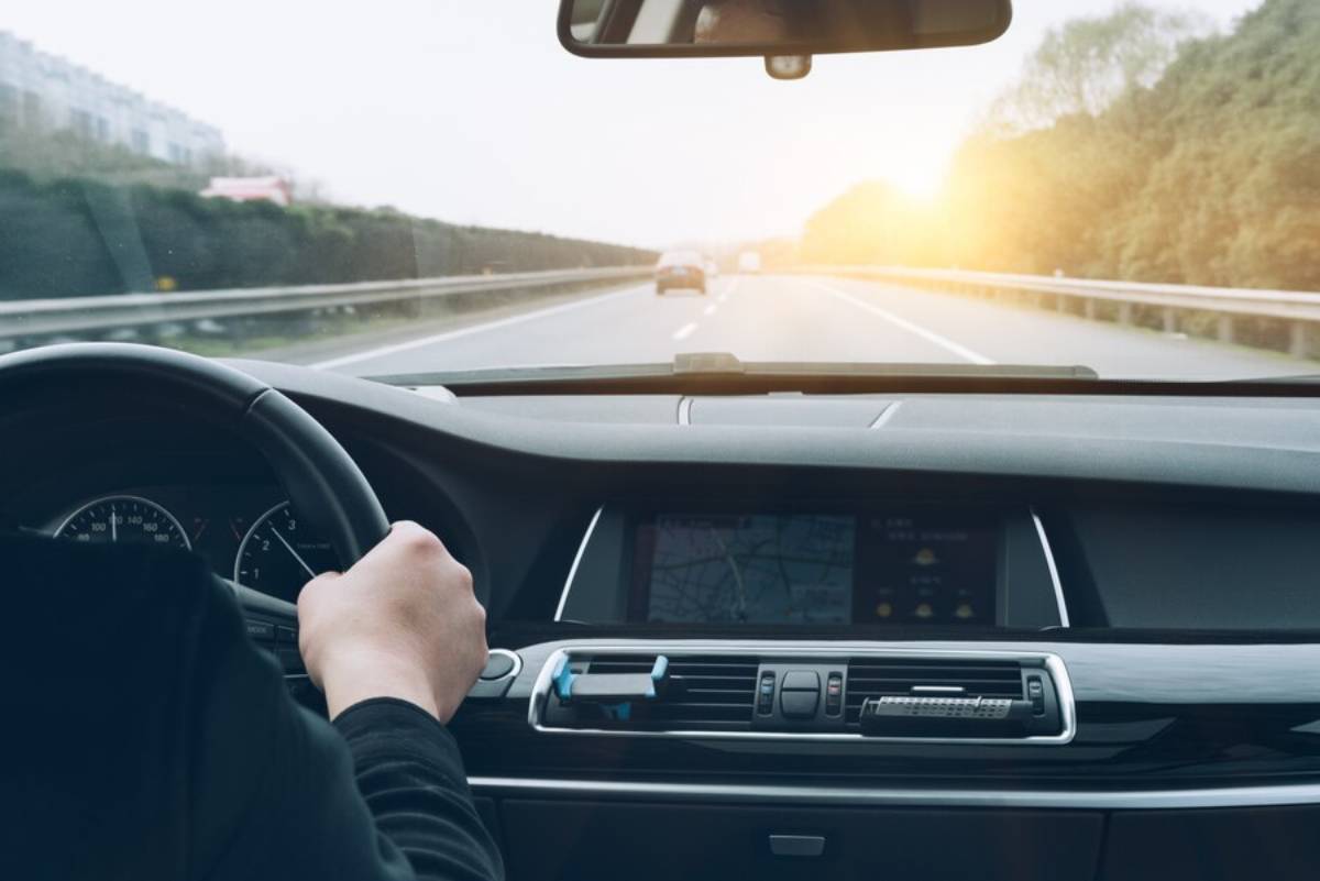  . A person driving a car on a highway, with the sun setting in the background, casting a warm glow over the scene.