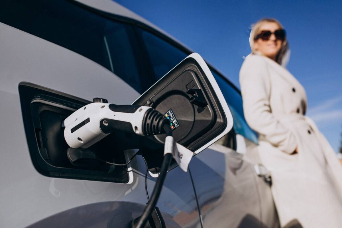   A woman connects a charging cable to her electric vehicle at a charging station.
 