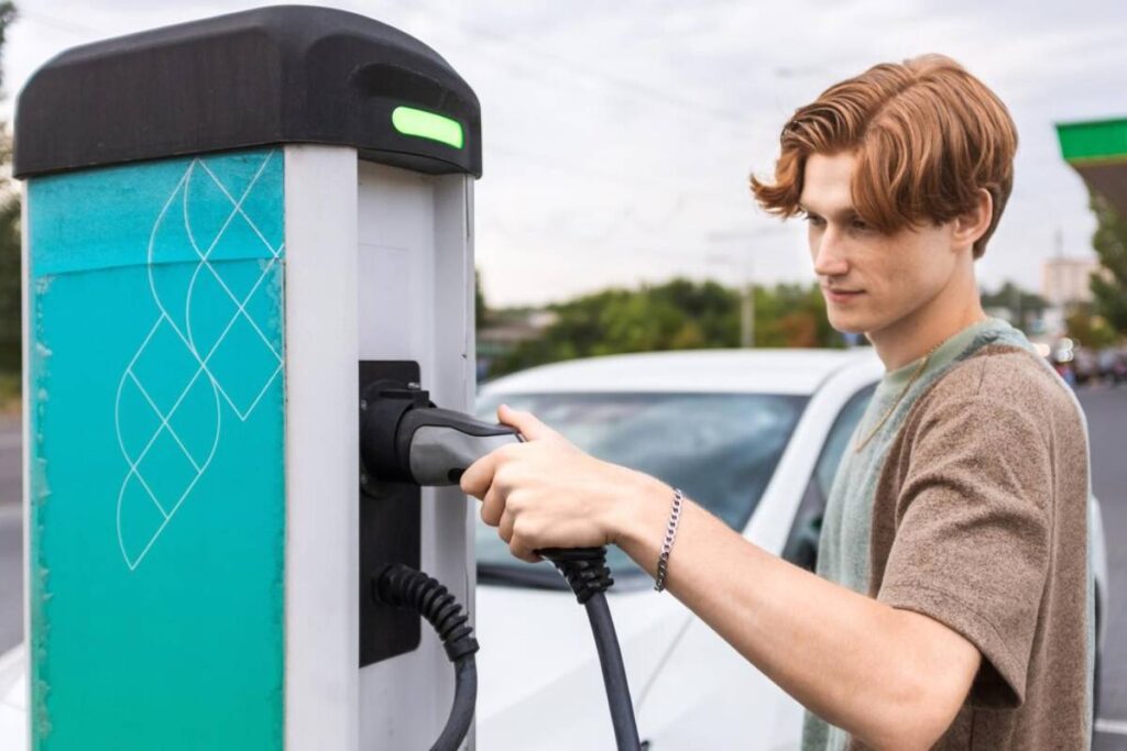 A man connects an electric car to a charging station, preparing to recharge the vehicle's battery.